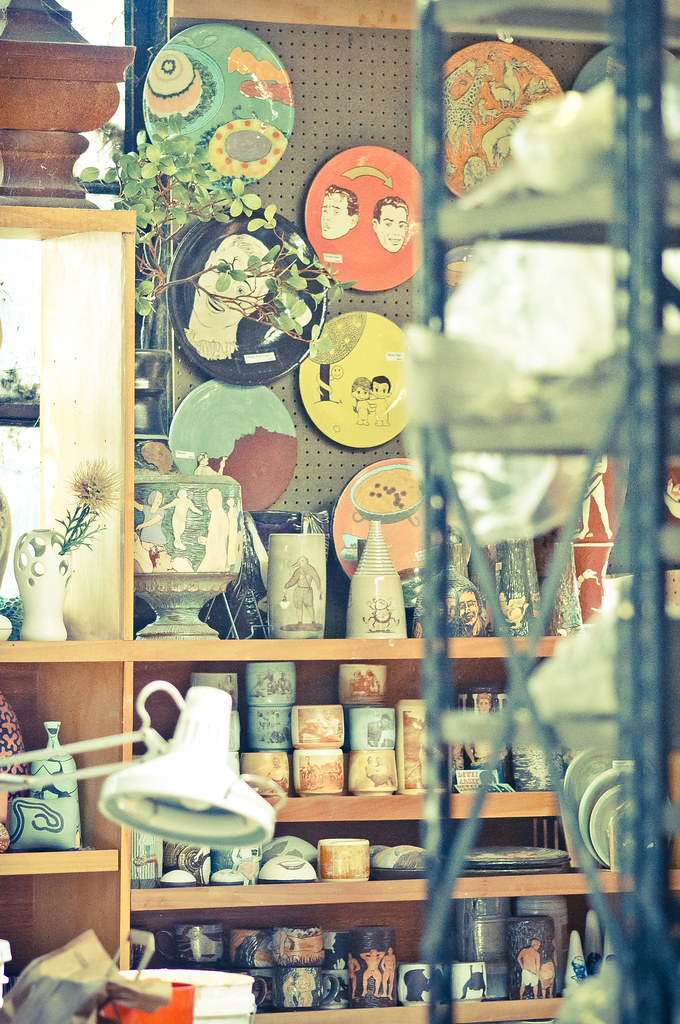 Studio shelves crowded with finished stoneware — vases, bowls and a raku-glazed jar.