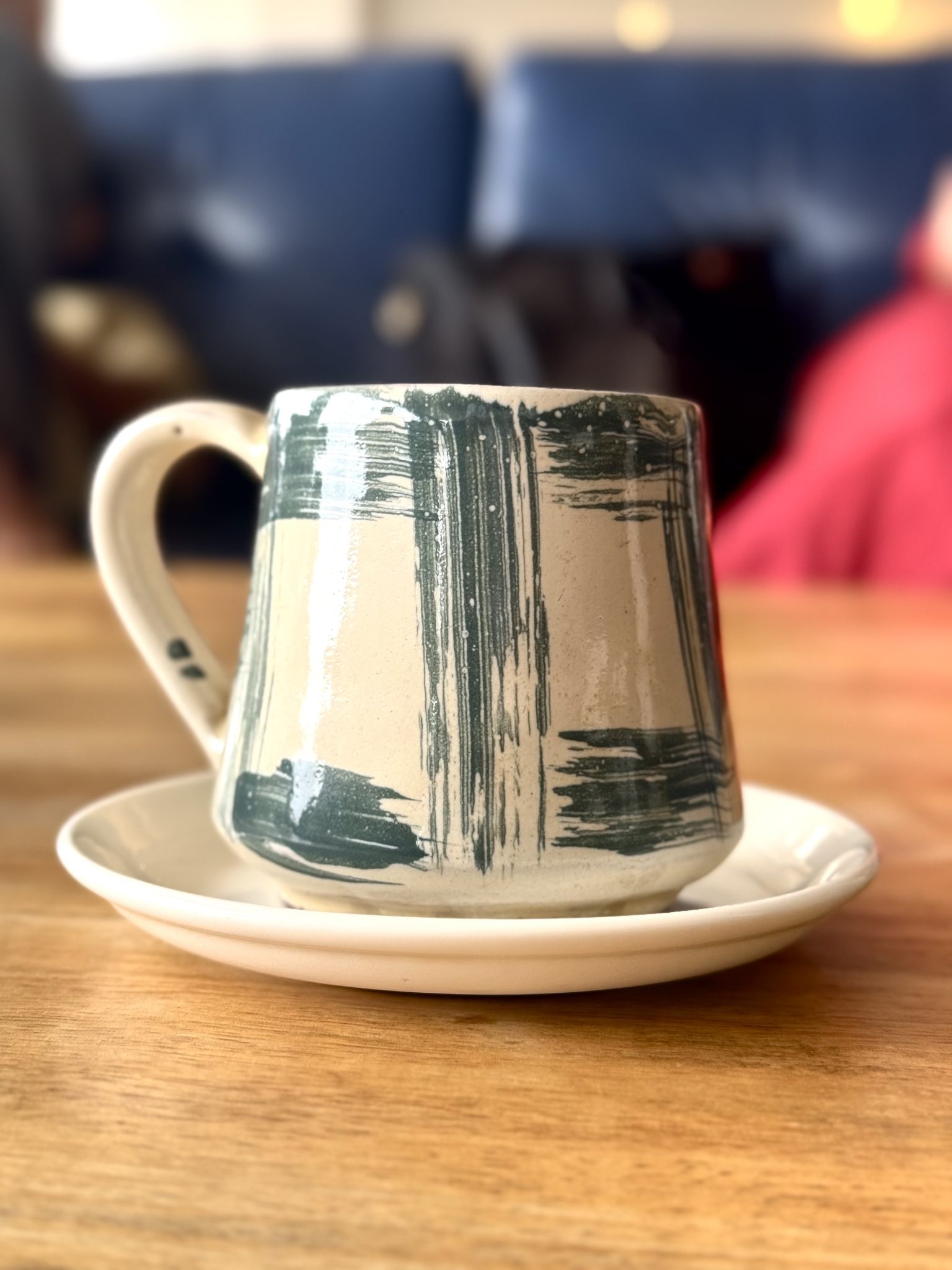 A handmade stoneware mug with dark green brushed glaze, on a matching saucer.