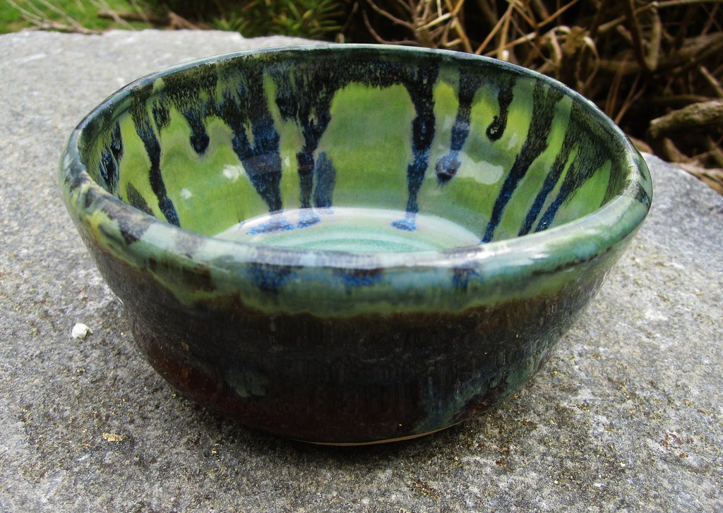 A hand-thrown bowl with a green and blue glaze running down its inside wall.